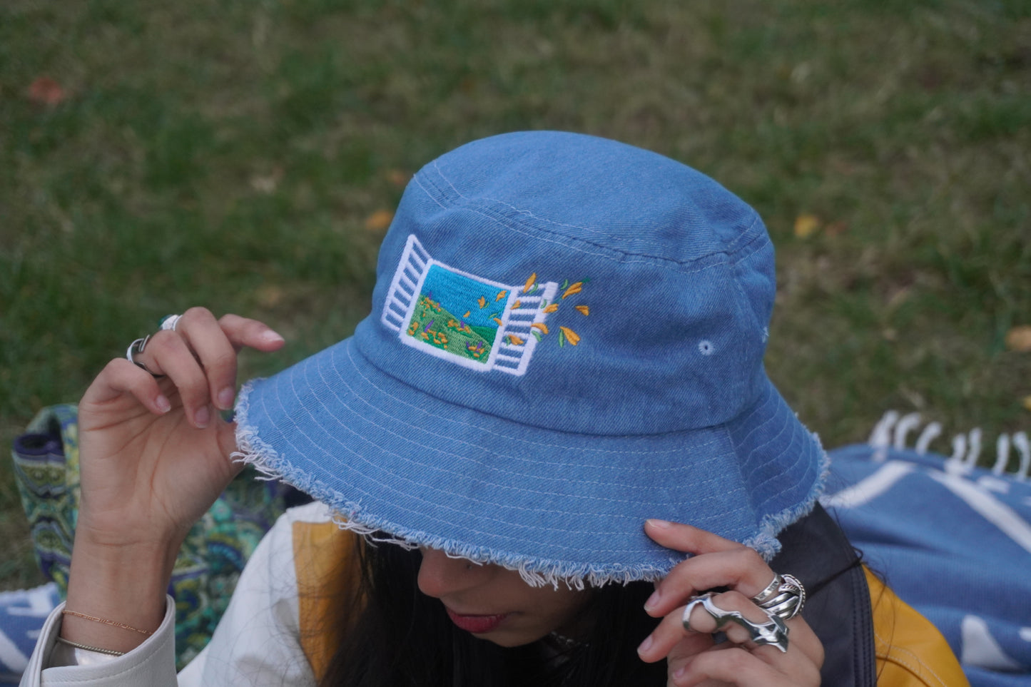 Person wearing a blue bucket hat with embroidery, sitting outdoors on grass.
