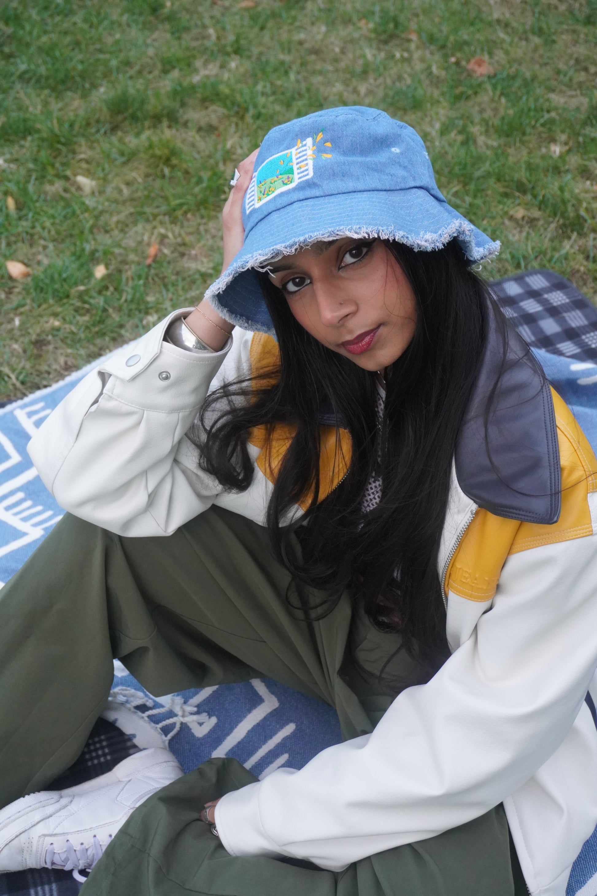 Person wearing a light blue bucket hat with embroidery, sitting on grass.