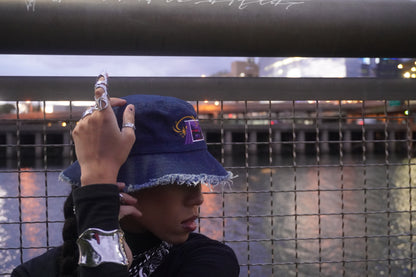 Person wearing a blue bucket hat with a logo, against a blurred background of water and lights.